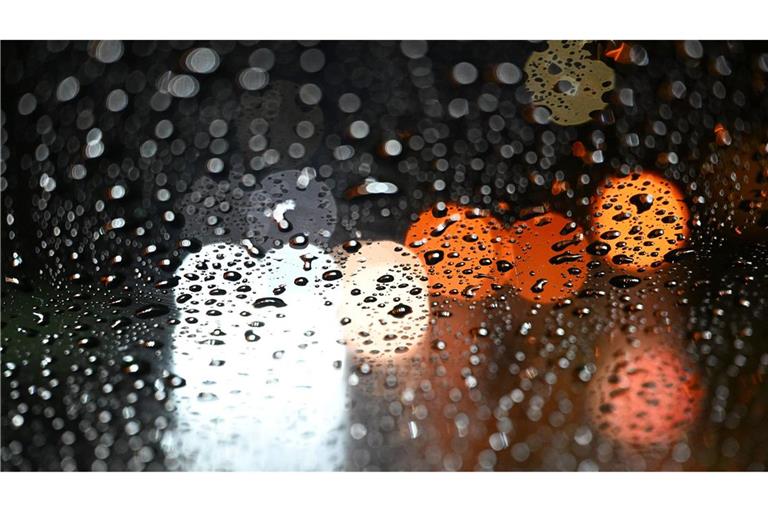 Stuttgart: Lichter von Fahrzeugen scheinen durch eine Autoscheibe, die mit Regentropfen bedeckt ist.