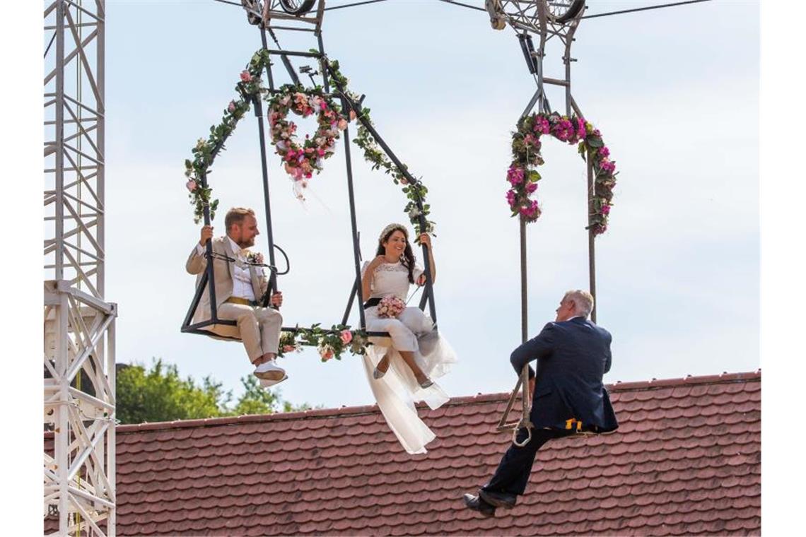 Artistin Anna Traber heiratet auf Hochseil Sven Lier (l-r), Braut Anna Traber sowie der Standesbeamte Oliver Rein sitzen in zwei Gestellen unter Motorrädern. Foto: Philipp von Ditfurth