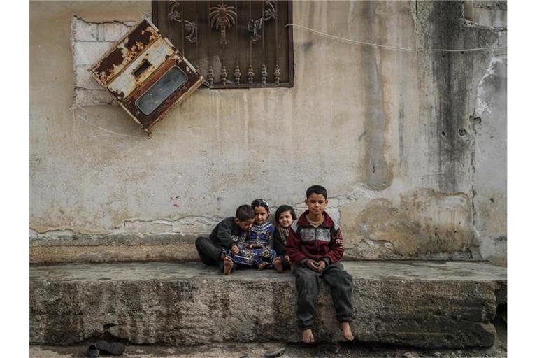 Syrische Kinder sitzen zwischen beschädigten Gebäuden im Dorf Afes. Rund zehn Jahre nach dem Beginn des Syrien-Konfliktes beklagt der UN-Menschenrechtsrat schwere Kriegsverbrechen in dem Krisenland. Foto: Anas Alkharboutli/dpa