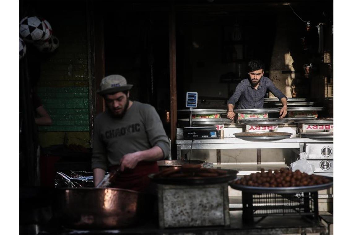 Syrische Verkäufer bereiten auf einem Straßenmarkt traditionelle Süßigkeiten zu. Foto: Anas Alkharboutli/dpa