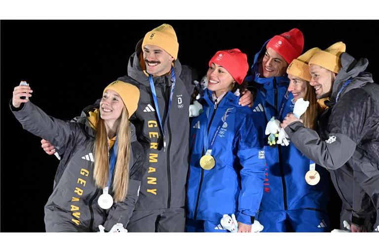 Tabitha Stoecker (Großbritannien) und Matt Weston (Großbritannien, beide M) posieren bei der Siegerehrung ihren Goldmedaillen nach dem Skeleton-Team-Wettbewerb neben Susanne Kreher (Deutschland, l) und Axel Jungk (Deutschland, 2.v.l.) mit der Silbermedaille und Jacqueline Pfeifer (Deutschland, 2.v.r.) und Christopher Grotheer (Deutschland) mit der Bronzemedaille bei den Olympischen Winterspielen Mailand Cortina 2026.