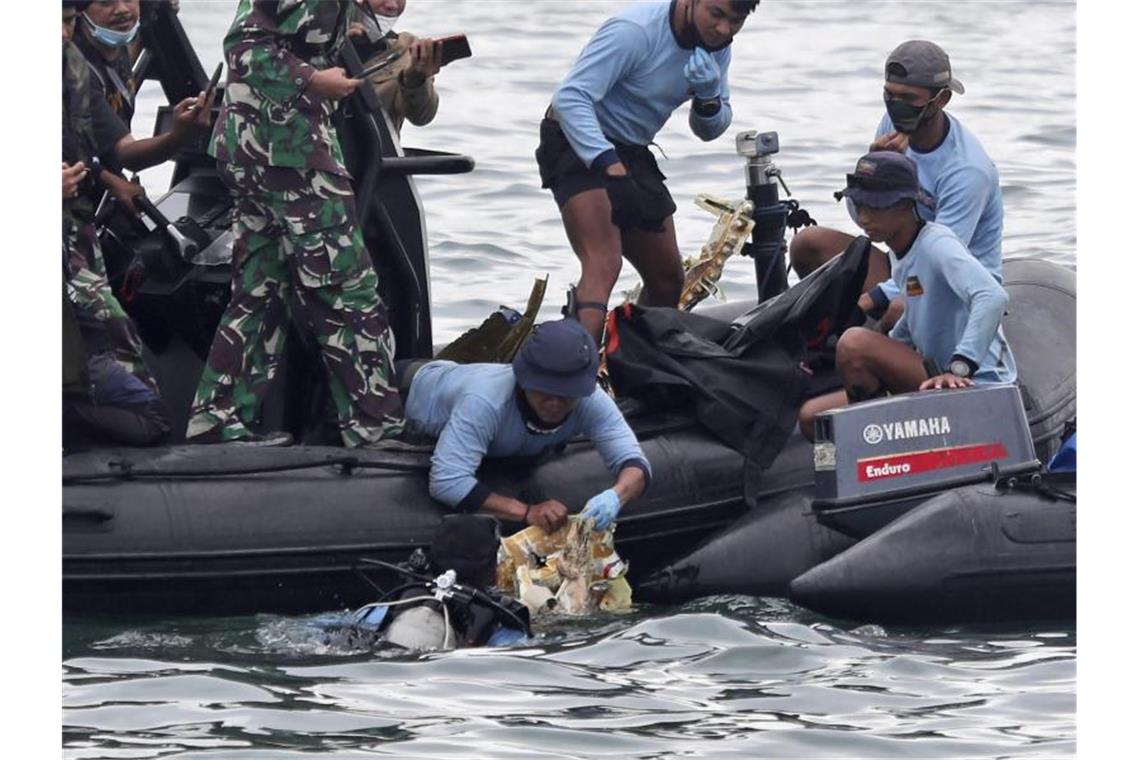 Taucher der indonesischen Marine ziehen ein Flugzeugteil aus dem Wasser. Foto: Achmad Ibrahim/AP/dpa