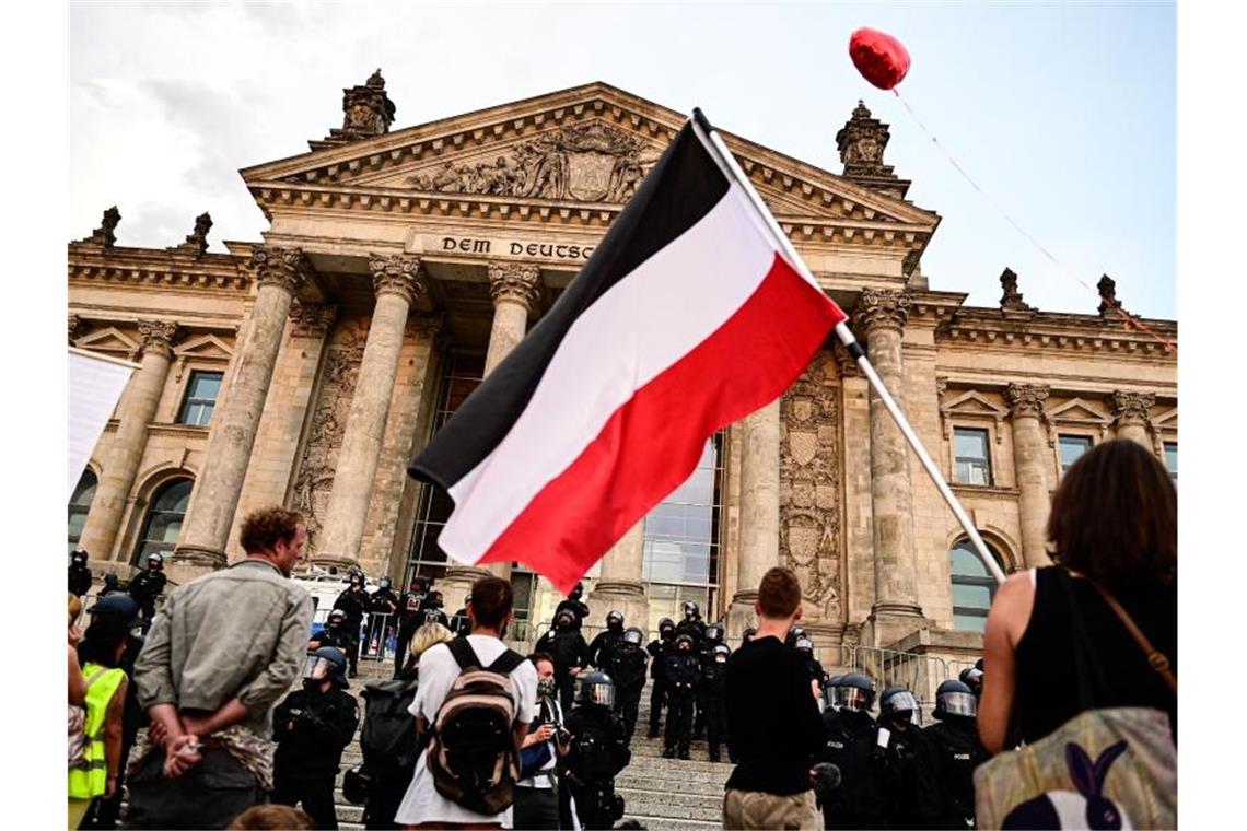 Teilnehmer einer Kundgebung gegen die Corona-Maßnahmen stehen vor dem Reichstag, ein Teilnehmer hält eine Reichsflagge mit schwarz-weiß-roten Querstreifen. Foto: Fabian Sommer/dpa