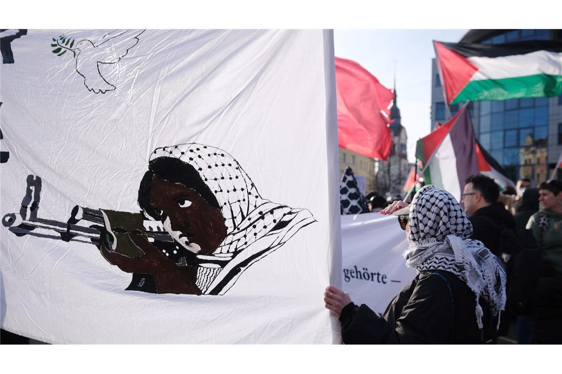 Teilnehmer einer propalästinensischen Demonstration stehen an einer Kreuzung im Stadtteil Connewitz in Leipzig und halten Fahnen und Transparente.