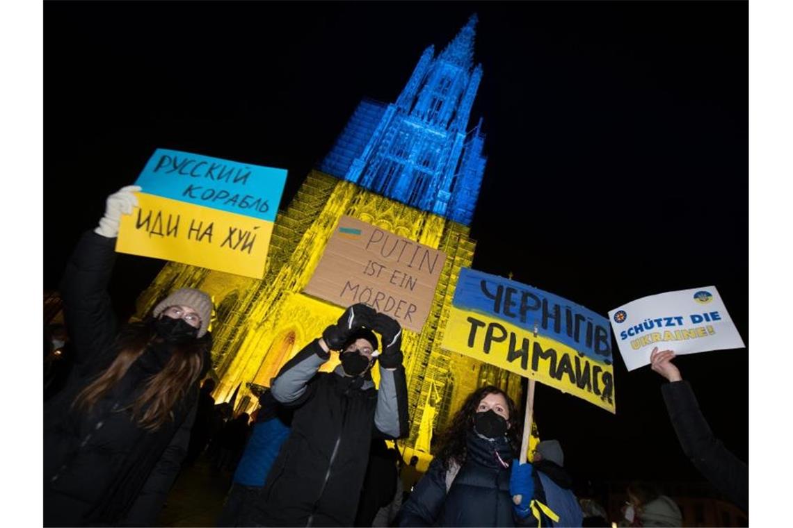 Solidarität: Ulmer Münsterturm in ukrainischen Landesfarben Teilnehmer eines Friedensgebetes halten vor dem Ulmer Münster Protestschilder hoch. Foto: Stefan Puchner/dpa