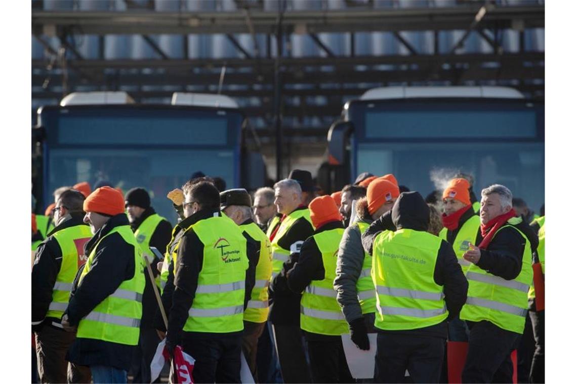 Teilnehmer eines Warnstreiks stehen vor Bussen. Foto: Marijan Murat/dpa/Archivbild