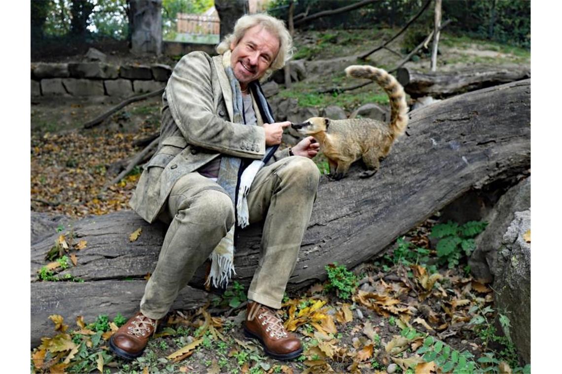 Thomas Gottschalk und Nasenbär „Thommy“ sitzen im Karlsruher Zoo auf einem Baumstamm. Foto: Timo Deible/Zoo Karlsruhe/dpa