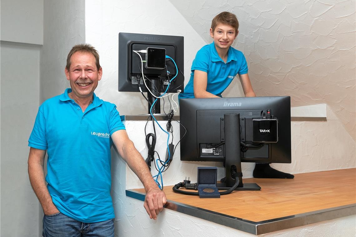 Thomas Leuprecht (links) zeigt mit seinem Sohn Janne (rechts) den Unterschied: Der Bildschirm rechts ist mit seinem „Mini-PC Cable-Caddy“ ausgestattet und die Kabel sind im Gehäuse aufgeräumt – ganz anders als beim Monitor oben links mit dem üblichen Kabelsalat. Foto: J. Fiedler