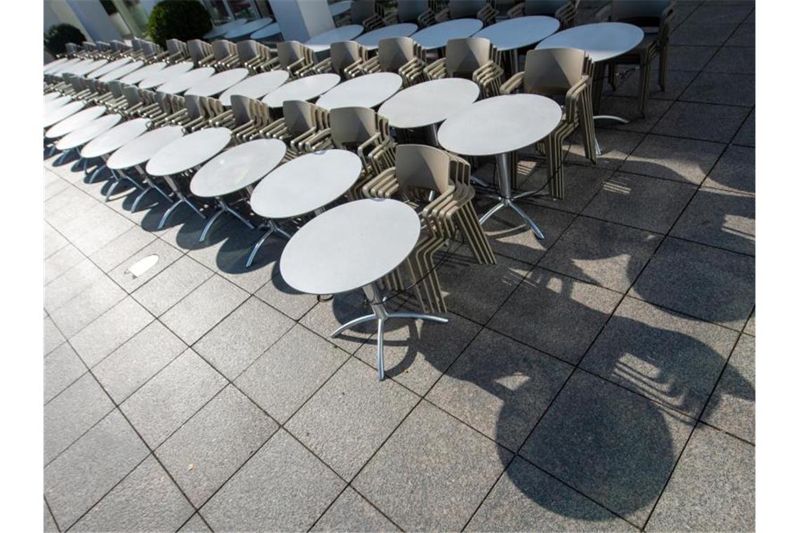 Tische und Stühle eines Straßencafes sind in der Sonne aufgereiht. Foto: Stefan Puchner/dpa/Symbolbild