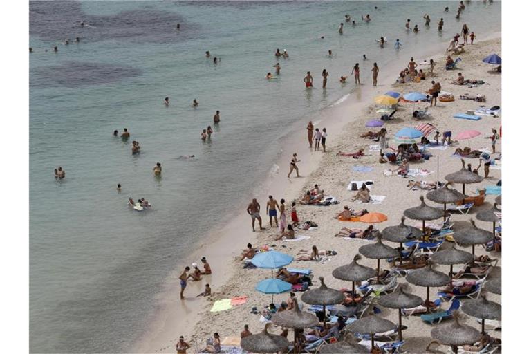 Touristen genießen an einem Strand bei Puerto Portals auf Mallorca die Sonne und das Meer. Der Klimawandel stellt die Reisebranche vor neue Herausforderungen. Foto: Clara Margais/dpa