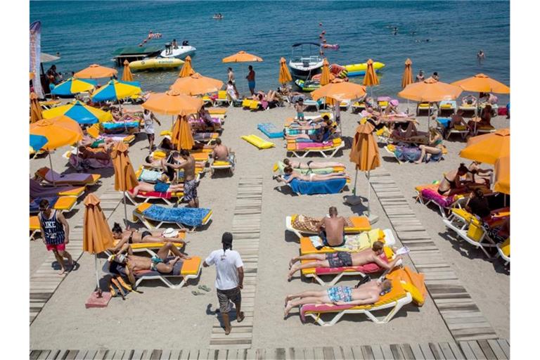 Touristen genießen die Sonne an einem Strand auf der griechischen Insel Kos. Foto: Santi Palacios/dpa