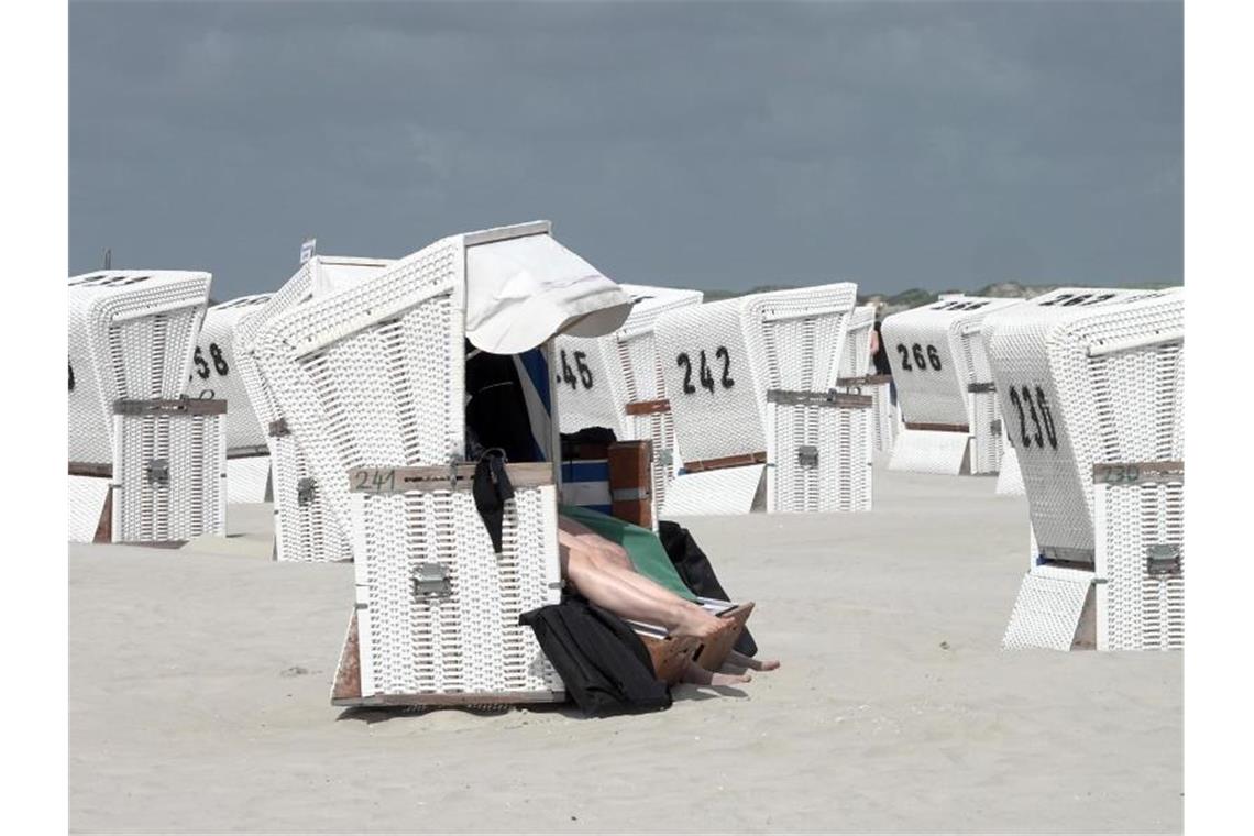 Touristen in einem Strandkorb am Strand von St. Peter-Ording. Foto: Bodo Marks/dpa