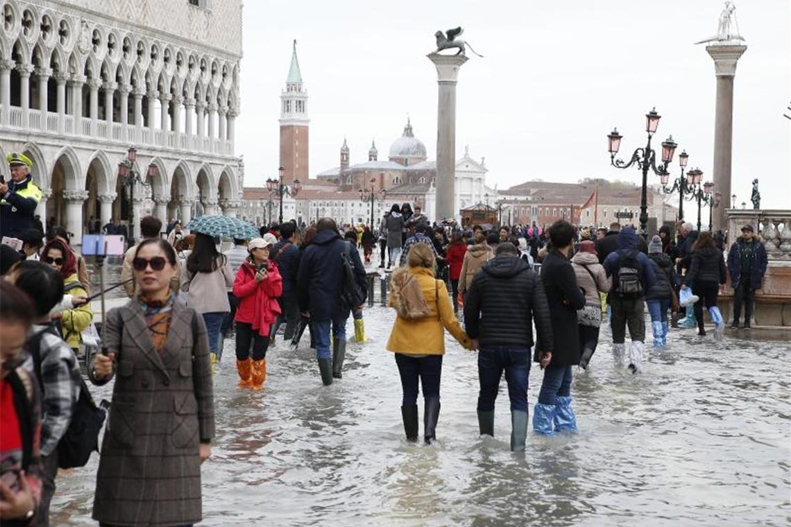 Touristen laufen auf dem überfluteten Markusplatz durch das Wasser. Foto: Andrea Gilardi/LaPresse via ZUMA Press/dpa