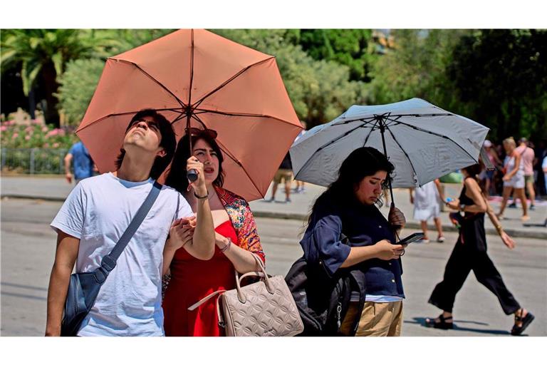 Touristen schützen sich an einem heißen Tag  mit Regenschirmen vor der Sonne (Symbolfoto).