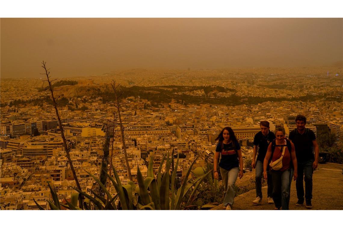 Touristen spazieren auf dem Lycabettus-Hügel in Athen, während der Himmel über der griechischen Hauptstadt mit dem antiken Akropolis-Hügel im Hintergrund infolge von Saharastaub eingetrübt ist.