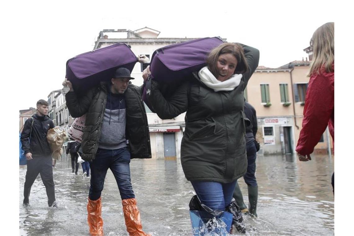 Touristen tragen ihr Gepäck durchs Hochwasser. Foto: Luca Bruno/AP/dpa