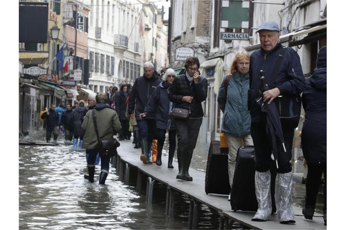 „Apokalyptische Zerstörung“: Hochwasser verwüstet Venedig Touristen ziehen ihr Gepäck über provisorische Gehsteige. Foto: Luca Bruno/AP/dpa