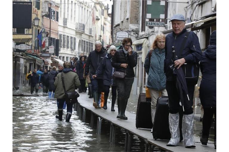 Touristen ziehen ihr Gepäck über provisorische Gehsteige. Foto: Luca Bruno/AP/dpa