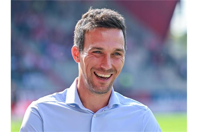 Trainer Christian Eichner von Karlsruhe steht lachend im Stadion. Foto: Armin Weigel/dpa/Archivbild