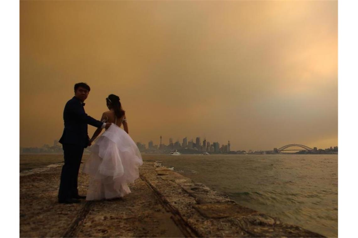Traumkulisse zum „schönsten Tag im Leben“? Keine Chance! Ein Brautpaar lässt sich vor der von Rauchschwaden verhangenen Skyline von Sydney fotografieren. Foto: Steven Saphore/AAP/dpa