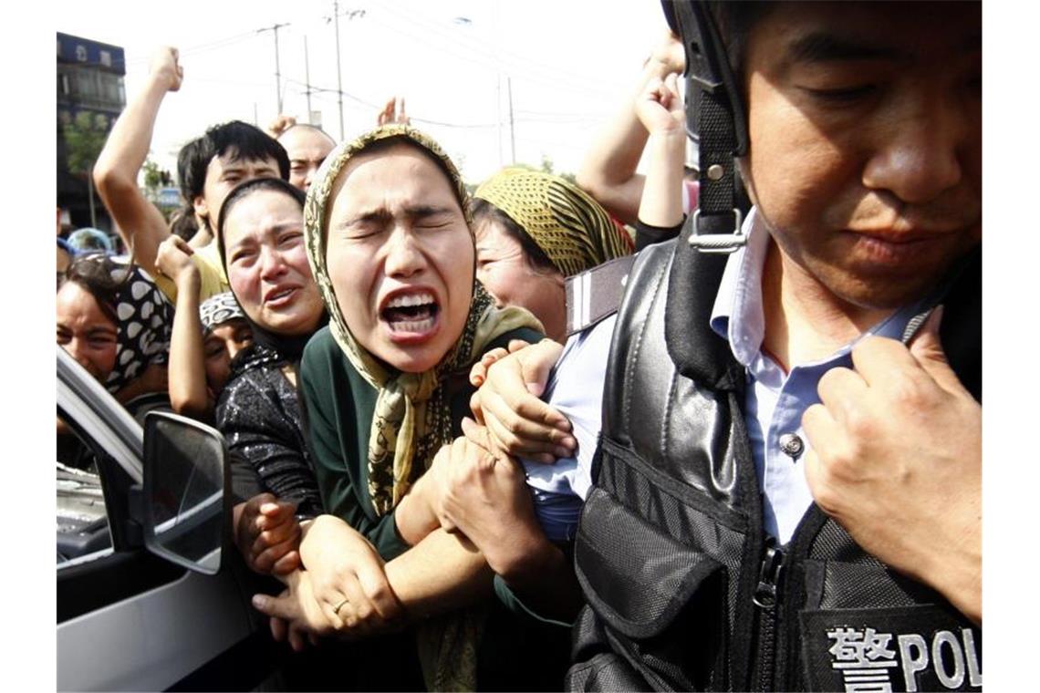 Uiguren rangeln bei einer Demonstration mit einem Polizisten. Foto: Oliver Weiken/dpa