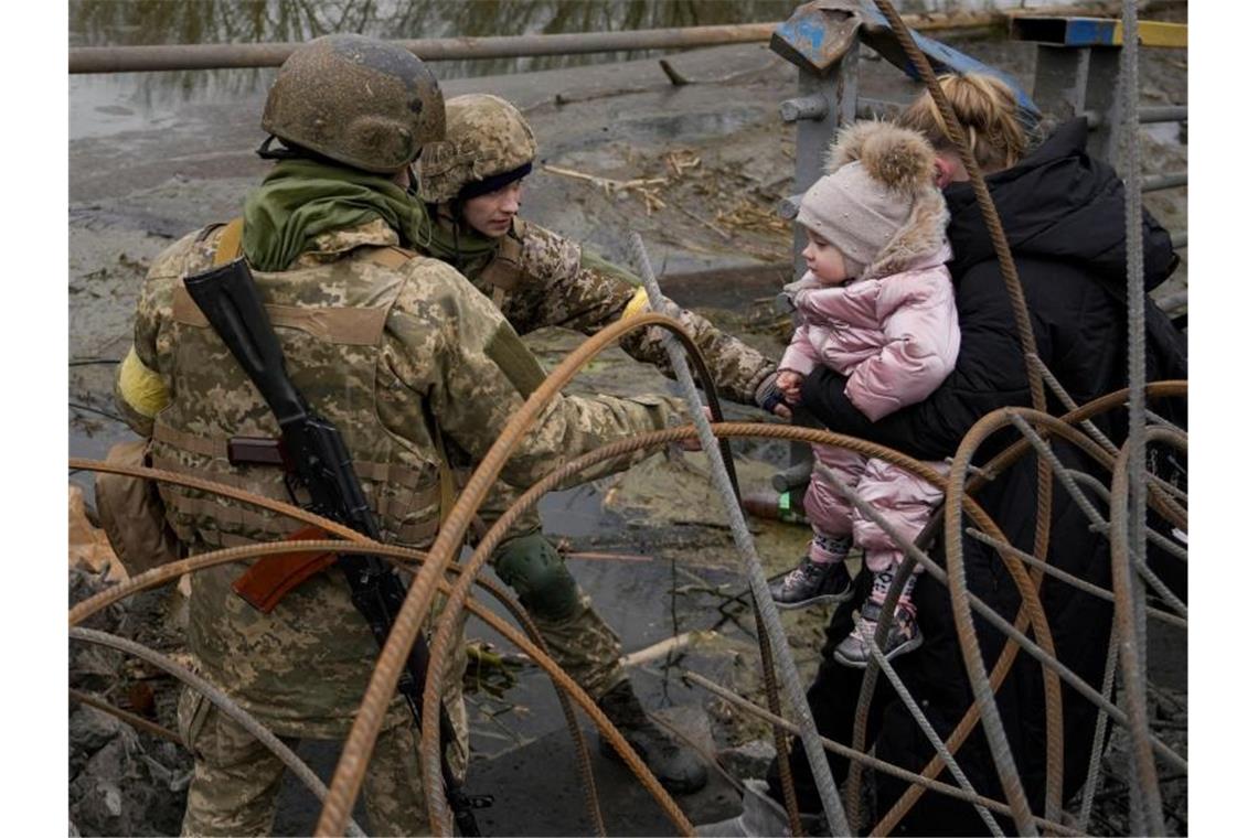 Russland setzt Angriff auf Mariupol fort Ukrainische Soldaten helfen einer Frau mit Kind, den Fluss Irpin zu überqueren. Foto: Vadim Ghirda/AP/dpa