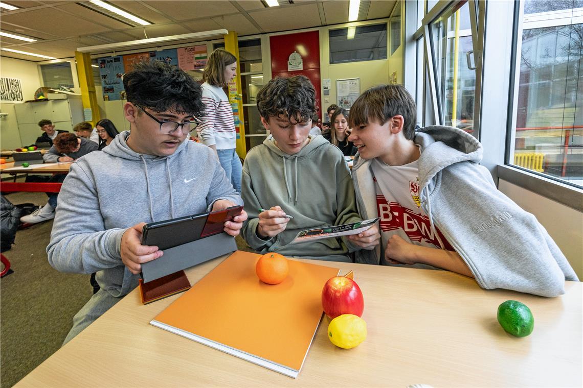 Um die KI zu trainieren, nehmen Klodian Hasani, Lars Pohl und Kjell Much (von links) ungefähr 100 Fotos von jedem Stück Plastikobst auf. Dadurch soll die KI die verschiedenen Obstsorten auch vor unterschiedlich farbigen Hintergründen erkennen. Foto: Dietmar van der Linden