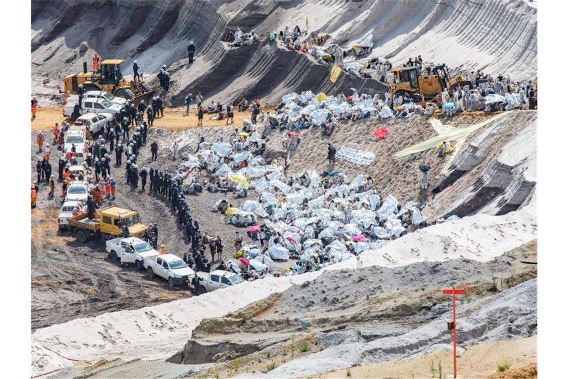 Umweltaktivisten schützen sich mit Rettungsdecken vor der Sonne, nachdem sie im Tagebau Garzweiler von Polizisten eingekesselt wurden. Foto: Marcel Kusch