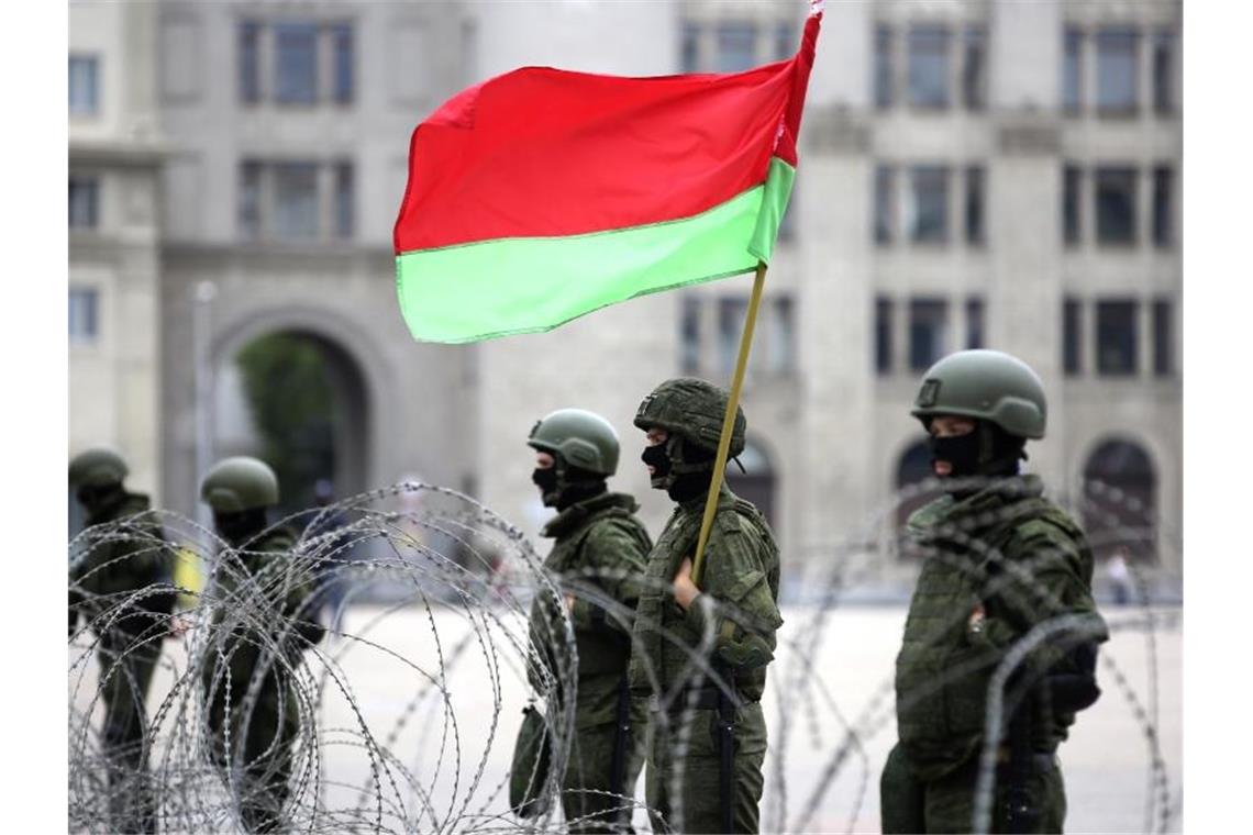 Uniformierte Sicherheitskräfte stehen in Minsk mit der belarussischen Staatsflagge hinter Stacheldraht. Foto: Uncredited/Tut.by/AP/dpa