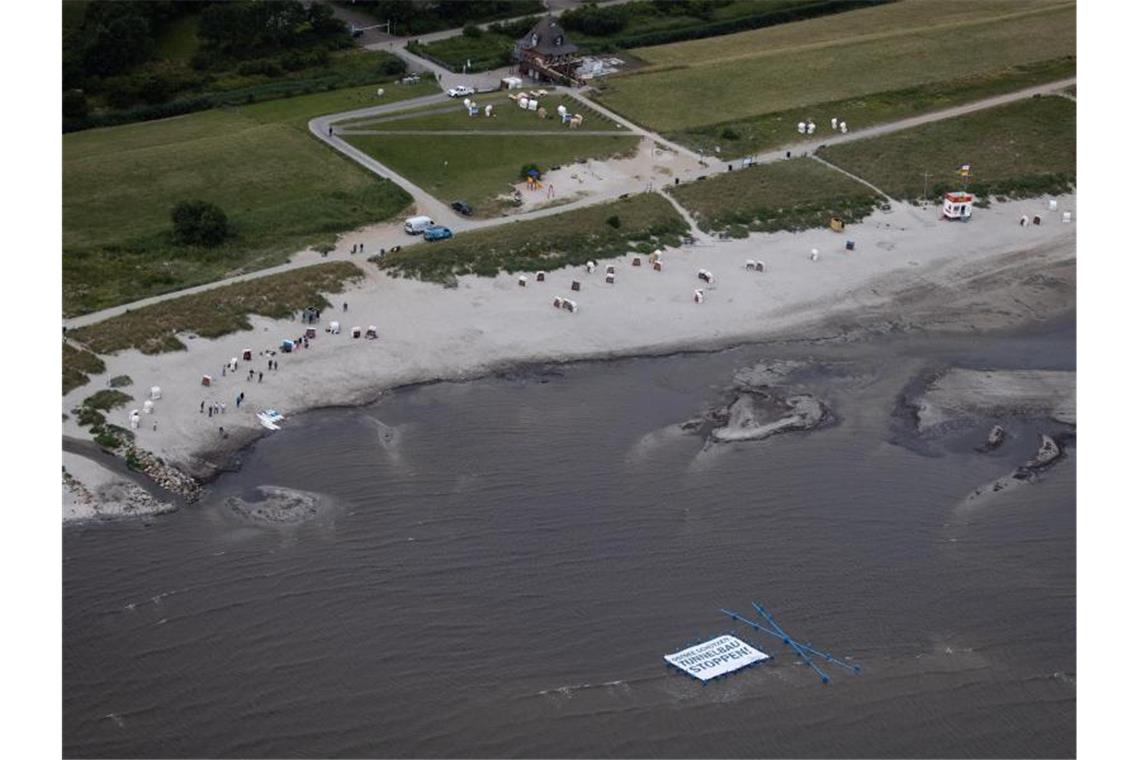 Wassersportler protestieren gegen Fehmarnbelt-Tunnel Unterstützer und Aktivisten der Protestaktion "Beltretter" halten ein Banner mit dem Text "Ostsee schützen. Tunnelbau stoppen!" und ein blaues Kreuz, während sie in der Ostsee am Naturschutzgebiet Grüner Brink nahe dem Fähranleger Puttgarden stehen. Foto: Christian Charisius/dpa