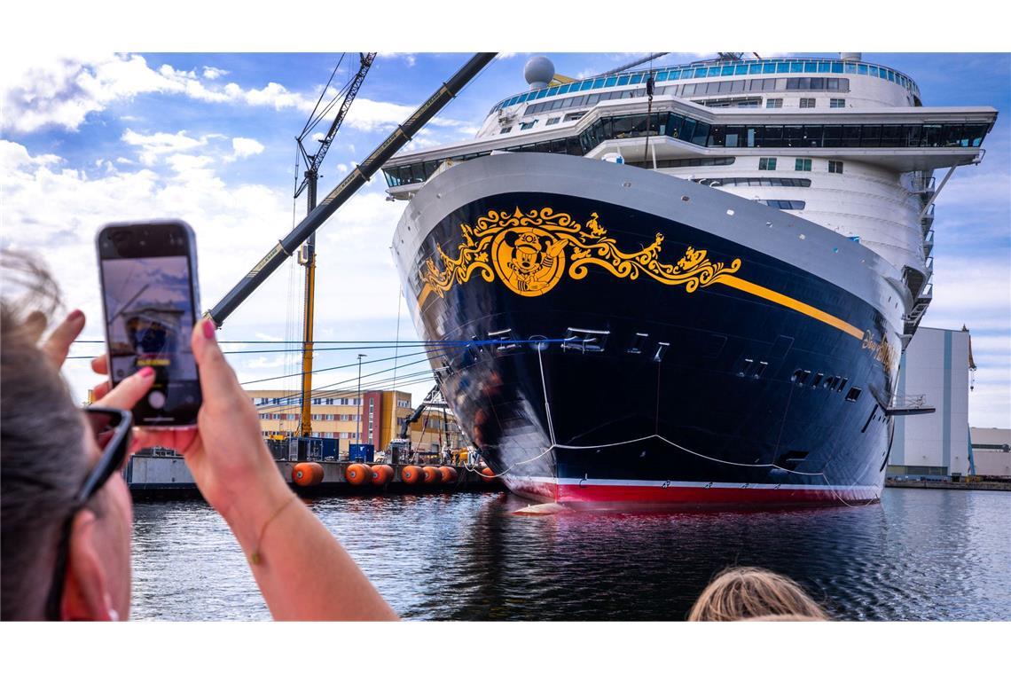 Urlauber fotografieren bei einer Hafenrundfahrt das neue Kreuzfahrtschiff „Disney Adventure“ am Ausrüstungskai der Wismarer Werft.
