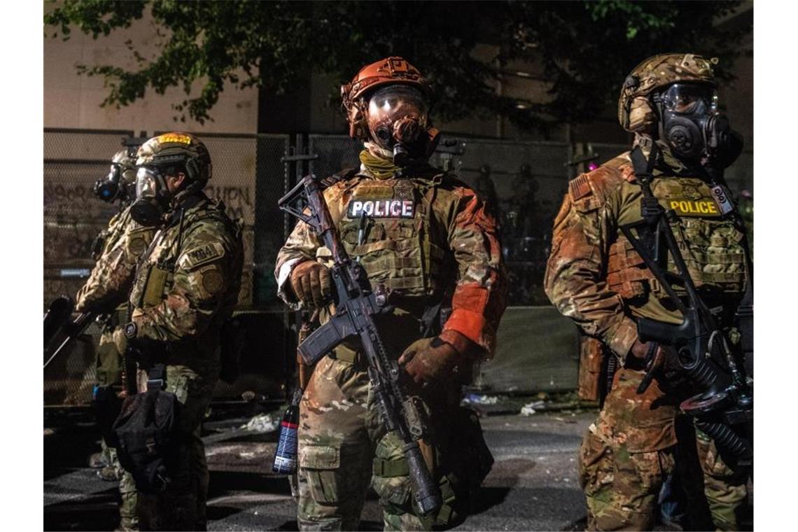 Proteste in Portland: Regierung kündigt härteres Vorgehen an US-Bundespolizisten stehen mit der Hand an der Waffe am Rande von Protesten in Portland. Foto: Imagespace/ZUMA Wire/dpa