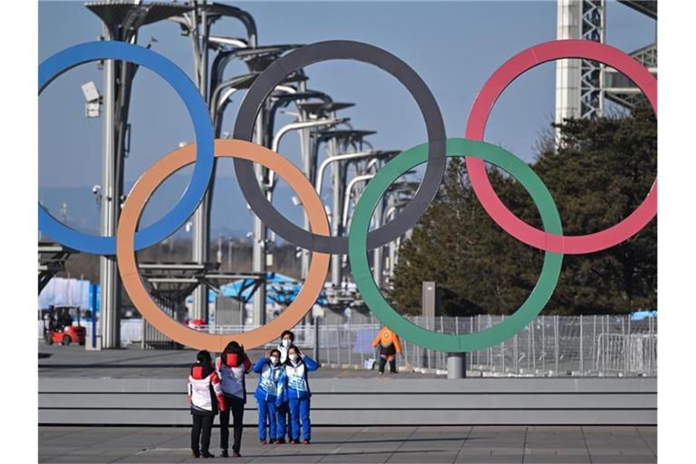 Von Olympia-Stimmung ist in Peking wenig zu spüren: Volunteers stehen vor den olympischen Ringen für ein Selfie. Foto: Peter Kneffel/dpa