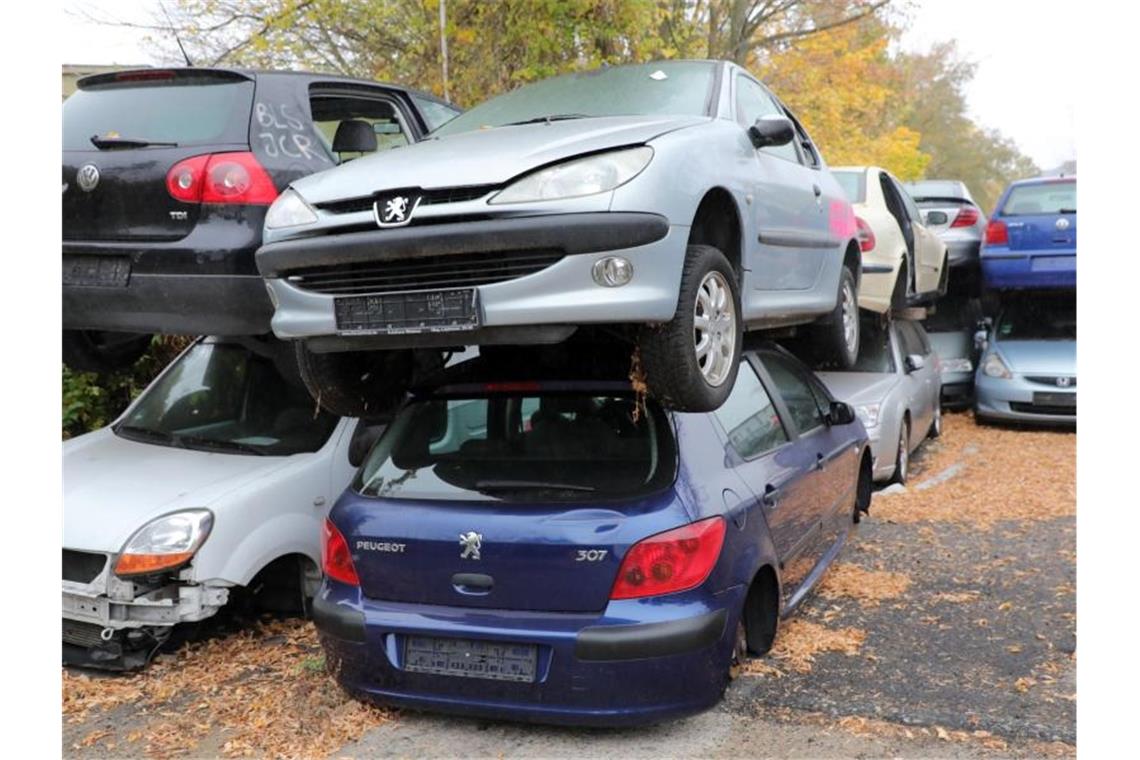 Vor dem Gelände eines Schrottplatzes mit Autopresse stapeln sich alte Autos, vorwiegend Dieselfahrzeuge. Foto: Wolfgang Kumm/dpa