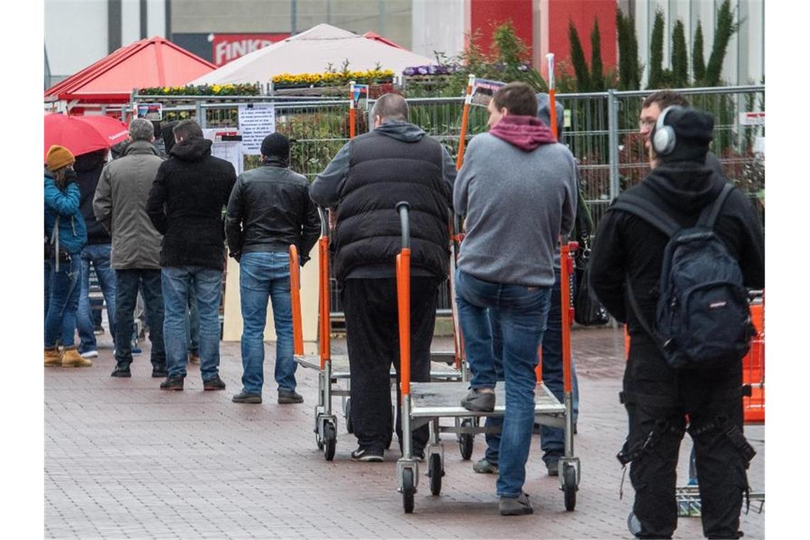 Vor einem Baumarkt stehen Menschen in einer Schlange. Foto: Stefan Puchner/dpa