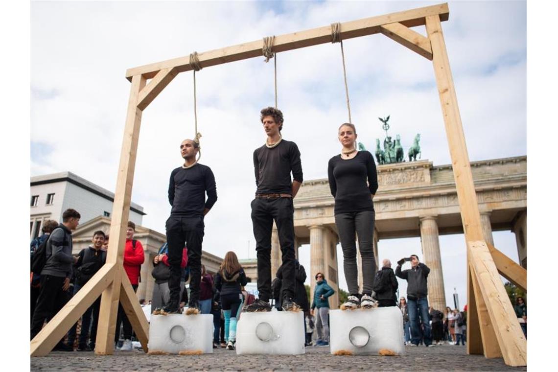 Vorm Brandenburger Tor: Drei Demonstranten stehen unter einem Galgen mit einem Seil um den Hals auf Eisblöcken. Foto: Tom Weller
