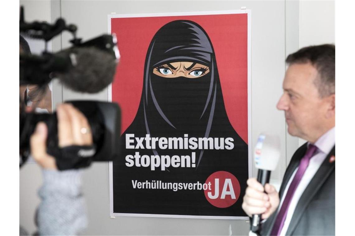 Walter Wobmann, Initiator der Initiative „Ja zum Verhüllungsverbot“, gibt neben einem Plakat mit der Aufschrift „Extremismus stoppen“ ein Interview. Foto: Peter Klaunzer/KEYSTONE/dpa