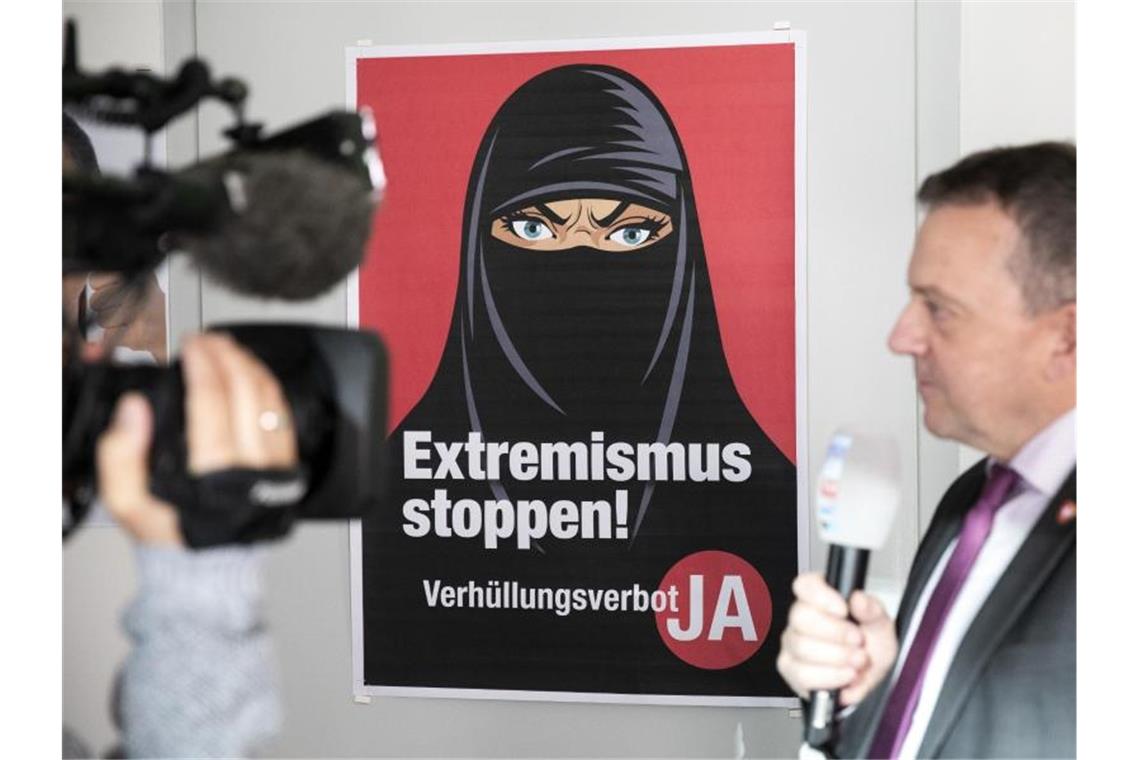Volksabstimmung: Schweizer beschließen Verhüllungsverbot Walter Wobmann, Initiator der Initiative „Ja zum Verhüllungsverbot“, gibt neben einem Plakat mit der Aufschrift „Extremismus stoppen“ ein Interview. Foto: Peter Klaunzer/KEYSTONE/dpa