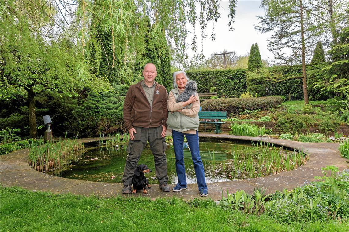 Waschbäreneinsätze dominieren in Murrhardt den Alltag Waschbären haben im Teich von Rosemarie Güllich (rechts) sämtliche Amphibien abgeräumt und im Garten Tieren wie Igeln zugesetzt. Stadtjäger Thomas Noack hat nun eine Falle aufgestellt und hofft, dass sich die Wasserfauna später wieder erholen kann. Auf seinen Einsätzen begleitet ihn sein Dackel Cesar, der sich mit Güllichs Bolli, einem Bolonka-Zwetna-Rüden, gut versteht. Fotos: Stefan Bossow