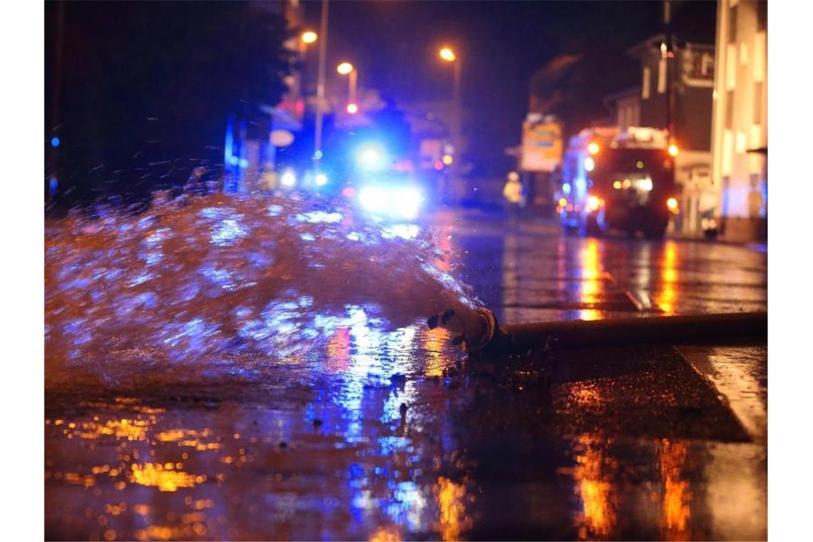 Überflutete Straßen nach Starkregen - Feuerwehrmann ertrinkt Wasser, das aus einem Keller in Erkrath gepumpt wurde, wird mit einem Feuerwehrschlauch auf die Straße geleitet. Foto: David Young/dpa