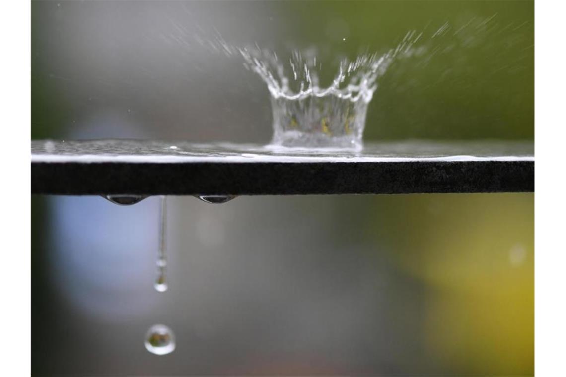 Wasser spritzt bei einem Regenschauer von der Wasseroberfläche auf einem Geländer in die Höhe. Foto: Patrick Seeger/Archivbild