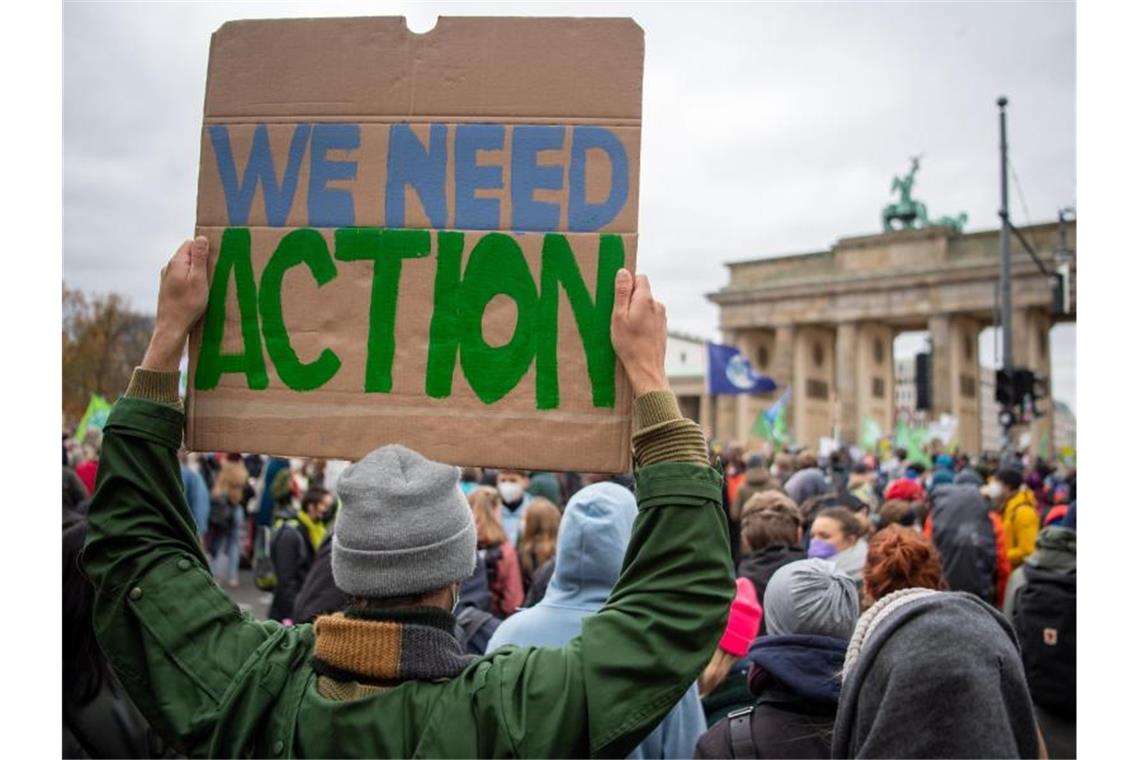 „We need Action“: Ein Teilnehmer mit einem Transparent vor dem Brandenburger Tor. Foto: Philipp Znidar/dpa