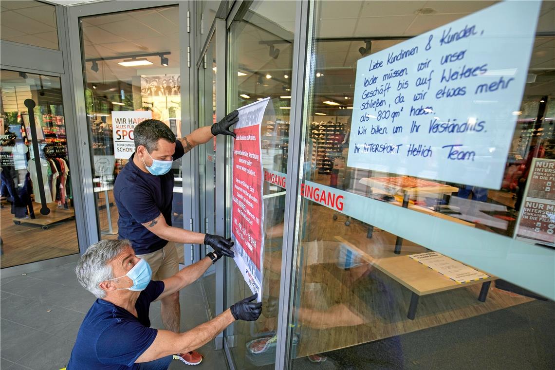 Wechselbad der Gefühle bei Intersport Hettich in Backnang: Erst hängten Jan Rössle (vorne) und Janos Kerekes Plakate an die Tür, um auf die Schließung hinzuweisen, dann freuten sie sich über die Nachricht, dass sie mit abgetrennten Teilflächen wieder öffnen dürfen. Foto: A. Becher