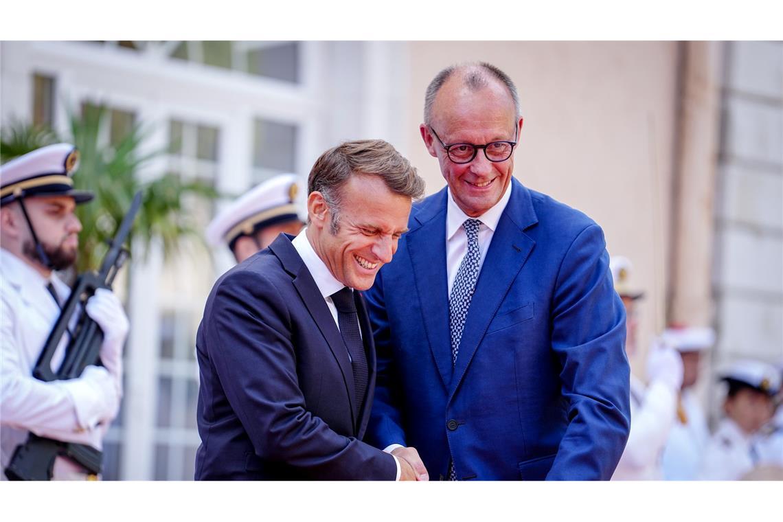 Wie zwei alte Freunde begrüßen sich Macron und Merz vor dem Fort du Cap Brun über der Cote d'Azur.