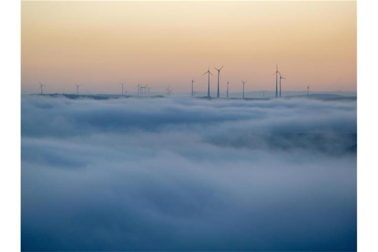 Windkraftanlegen im Hochwald ragen am Morgen aus dem Nebel, unter dem die Stadt Trier noch im Verborgenen liegt. Foto: Harald Tittel/dpa