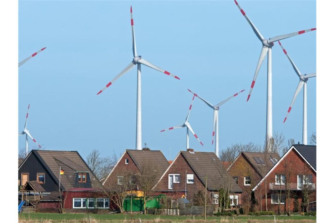 Windräder eines Windparks drehen sich dicht hinter einer Wohnsiedlung. Foto: Ingo Wagner/dpa