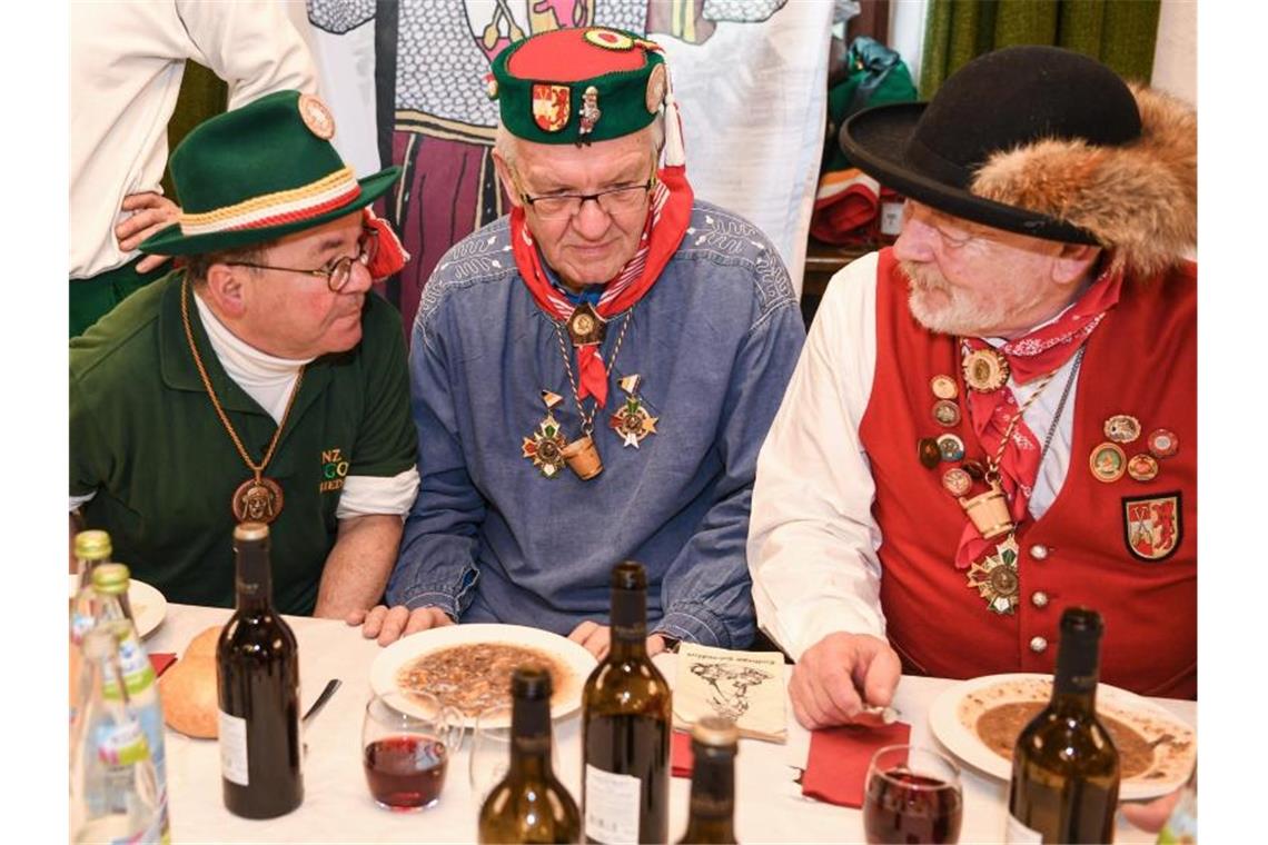 Winfried Kretschmann (Bündnis 90/Die Grünen, M), Ministerpräsident von Baden-Württemberg, sitzt am Fastnachtsdienstag mit anderen Narren im Rathaus vor seinen Froschkutteln. Daneben sitzen Vize-Zunftmeister Lothar Sauter (l) und Ehrenzunftmeister Peter Bucher (r). Foto: Felix Kästle/dpa