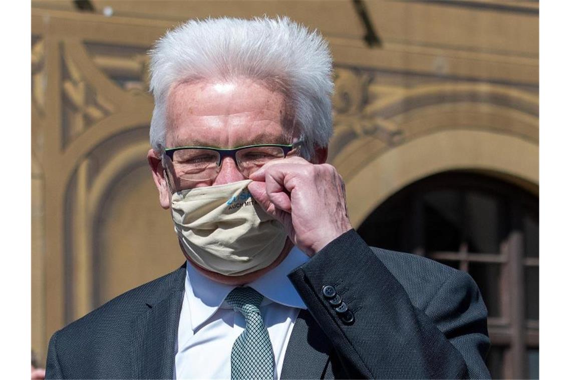 Winfried Kretschmann (Bündnis 90/Die Grünen) zieht sich eine Maske auf. Foto: Stefan Puchner/dpa/Archivbild