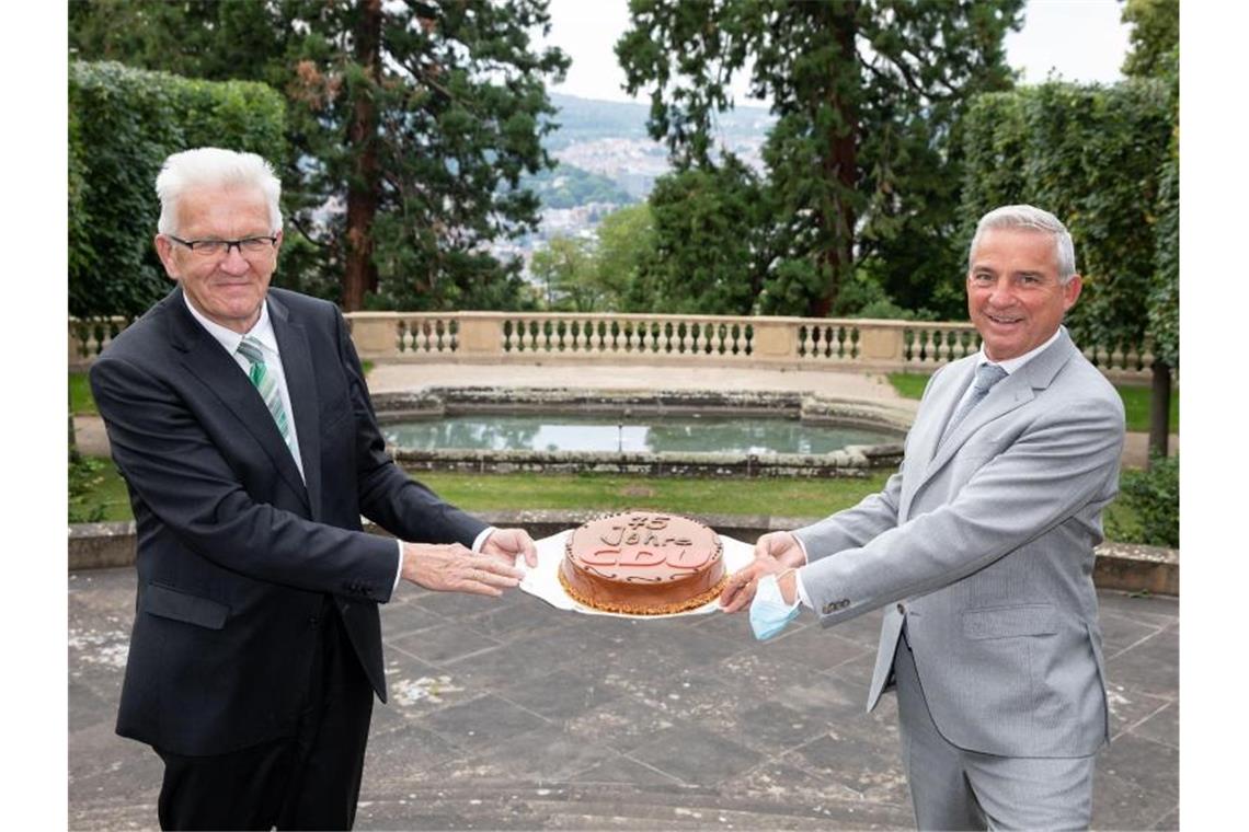 Winfried Kretschmann (l, Bündnis 90 / Die Grünen) überreicht Thomas Strobel (CDU) eine Torte zum 75-jährigen Bestehen der Partei CDU. Foto: Uli Regenscheidt/Staatsministerium Baden-Württemberg/dpa