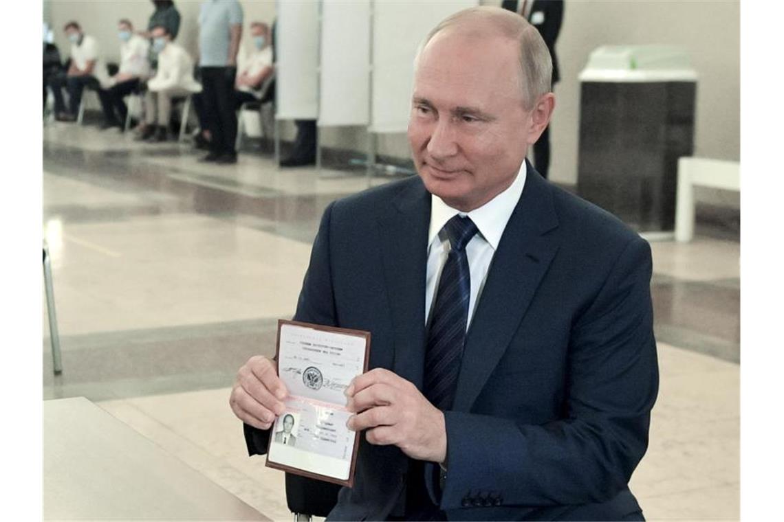 Kremlchef Putin feiert neue Verfassung für Machterhalt Wladimir Putin, Präsident von Russland, zeigt einer Mitarbeiterin der Wahlkommission seinen Pass in einem Wahllokal. Foto: Alexei Druzhinin/Pool Sputnik Kremlin/AP/dpa